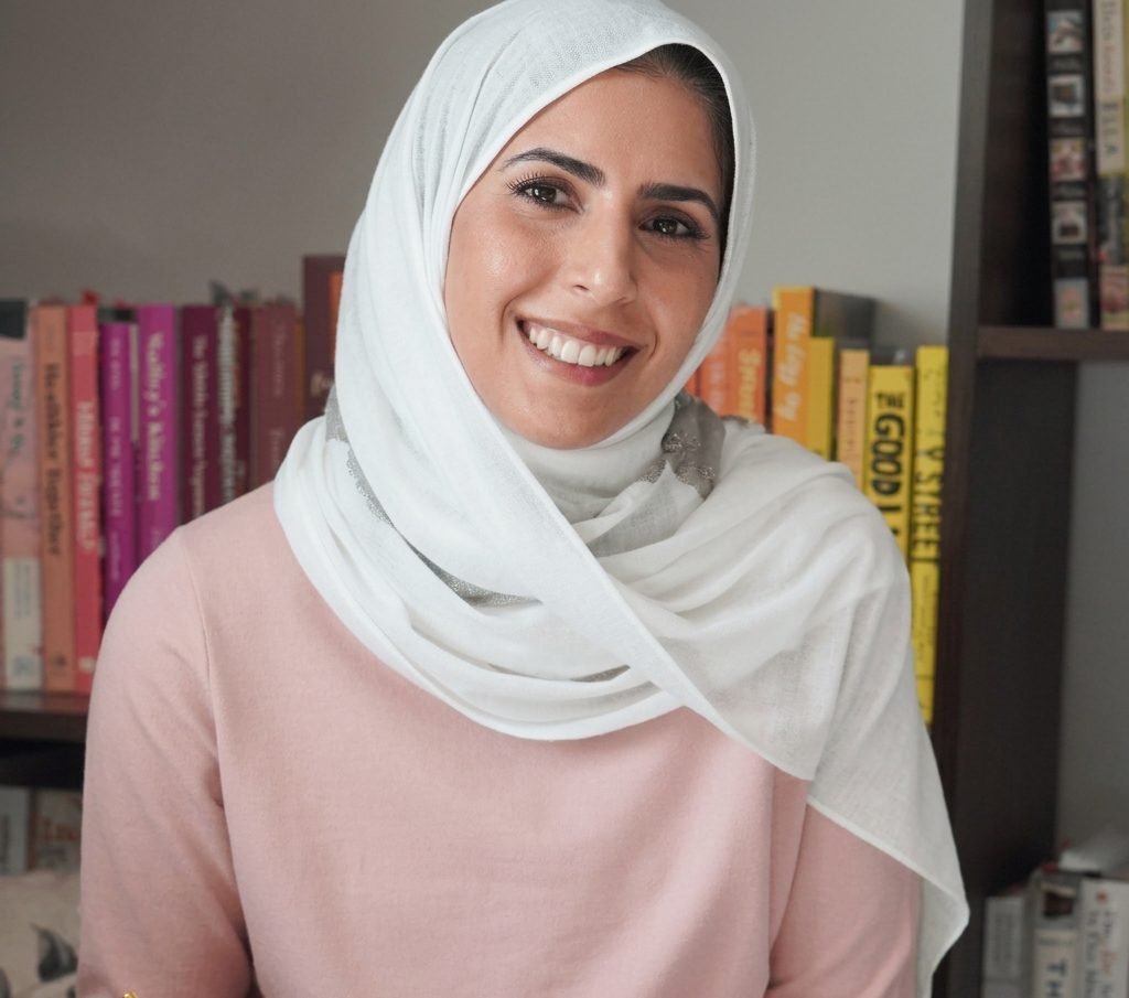 Portrait of Arwa sitting in front of a bookshelf